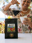 Person pouring coffee from a carafe into a cup next to a bag of Ali'i Kona Coffee.